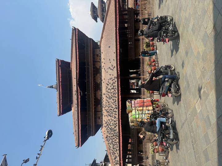 Traditional multi-tiered pagoda in Kathmandu Durbar Square with motorbikes passing by.