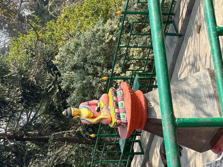 Colorful seated Buddha statue on a pedestal along a pathway lined with railings and greenery