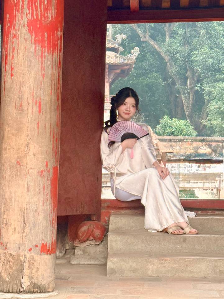 Young woman in traditional dress holding a folding fan by a red temple column.