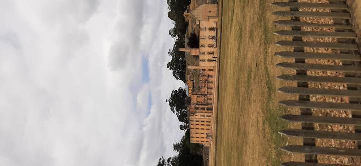 Historic sandstone penitentiary buildings across an open lawn under a cloudy Tasmanian sky.