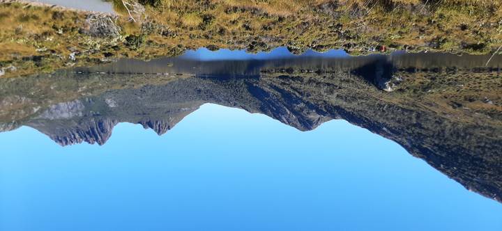 Crystal-clear lake surrounded by rugged peaks of Cradle Mountain under a bright blue sky.