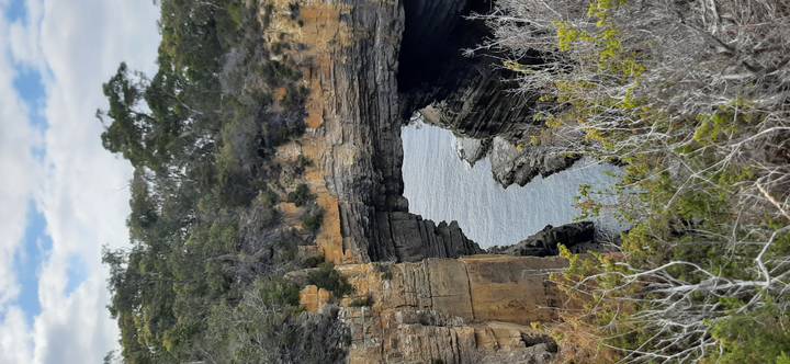 Dramatic coastal rock arch towers above the sea, framed by rugged vegetation.