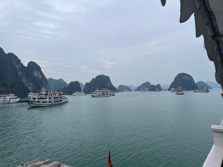 Calm turquoise bay dotted with cruise boats and limestone islets under a hazy sky.