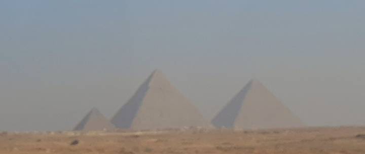Distant view of the pyramids in a hazy desert landscape.