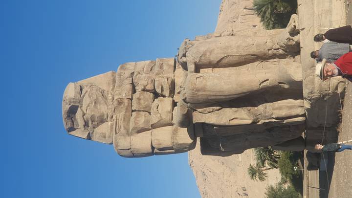 Colossal stone statue of the pharaoh at Luxor with blue sky backdrop and visitors nearby.