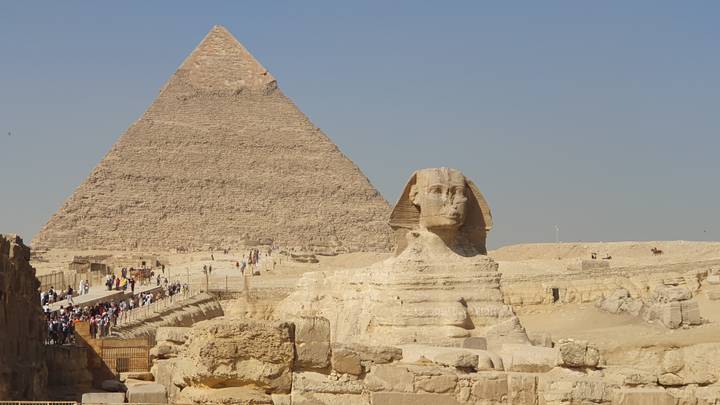 Iconic view of the Great Pyramid rising behind the Sphinx under a clear blue sky.