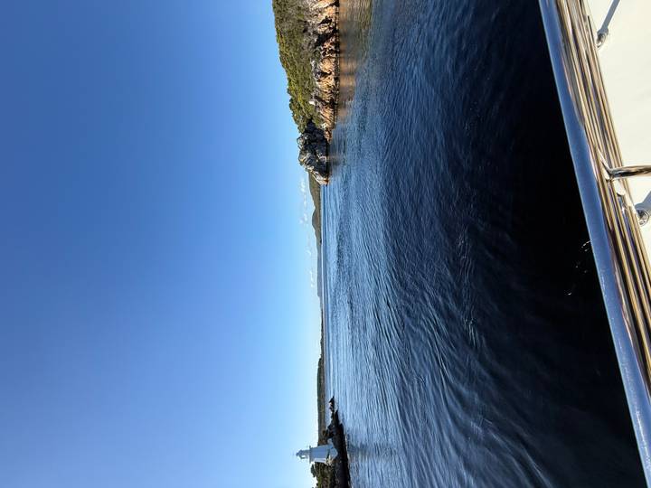 A calm river estuary stretches toward distant hills, viewed from the rail of a boat on a clear day.