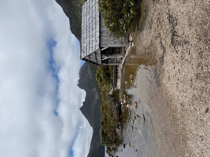 A rustic timber boathouse sits on the shore of Dove Lake beneath misty Cradle Mountain.