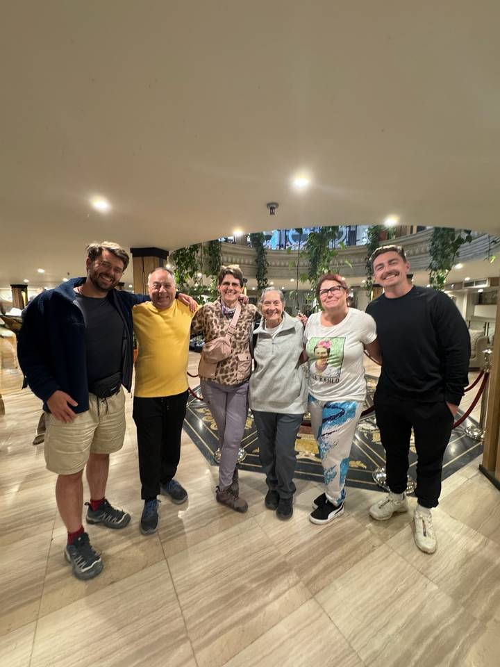 Smiling tour group posing together in an elegant hotel lobby with marble floors and hanging plants.