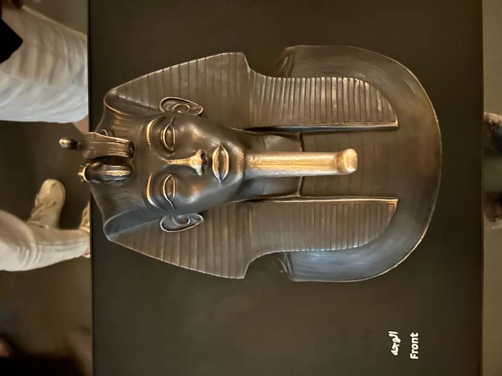 Ancient Egyptian pharaoh mask displayed in dimly lit museum exhibit.