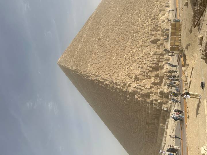 Majestic Great Pyramid of Giza towering over tourists gathered at its base on a hazy day.