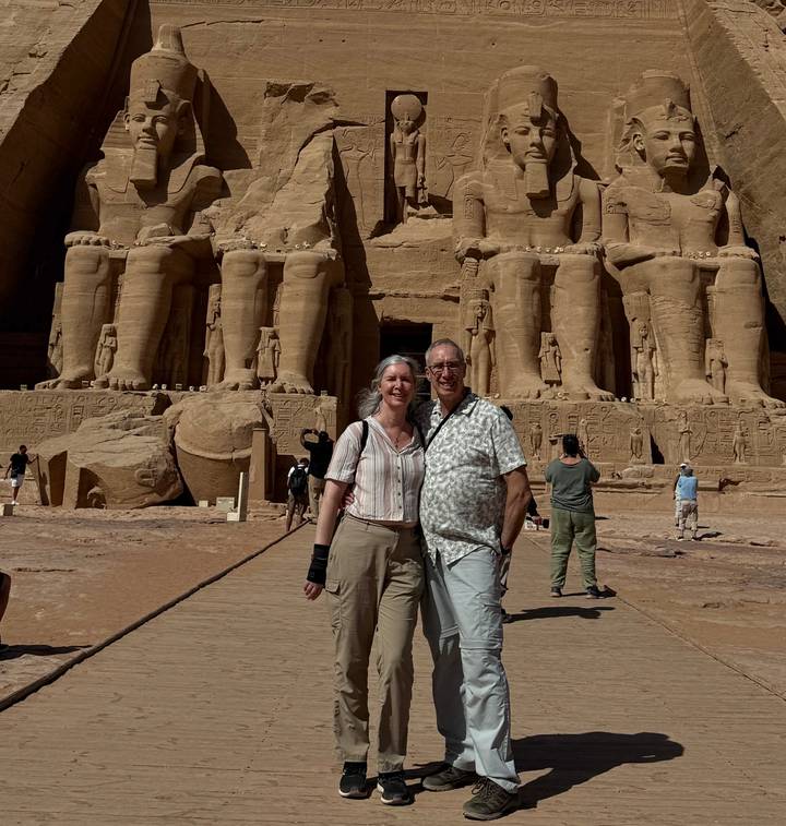 Smiling couple posing in front of the colossal statues of Abu Simbel temple under bright sun.