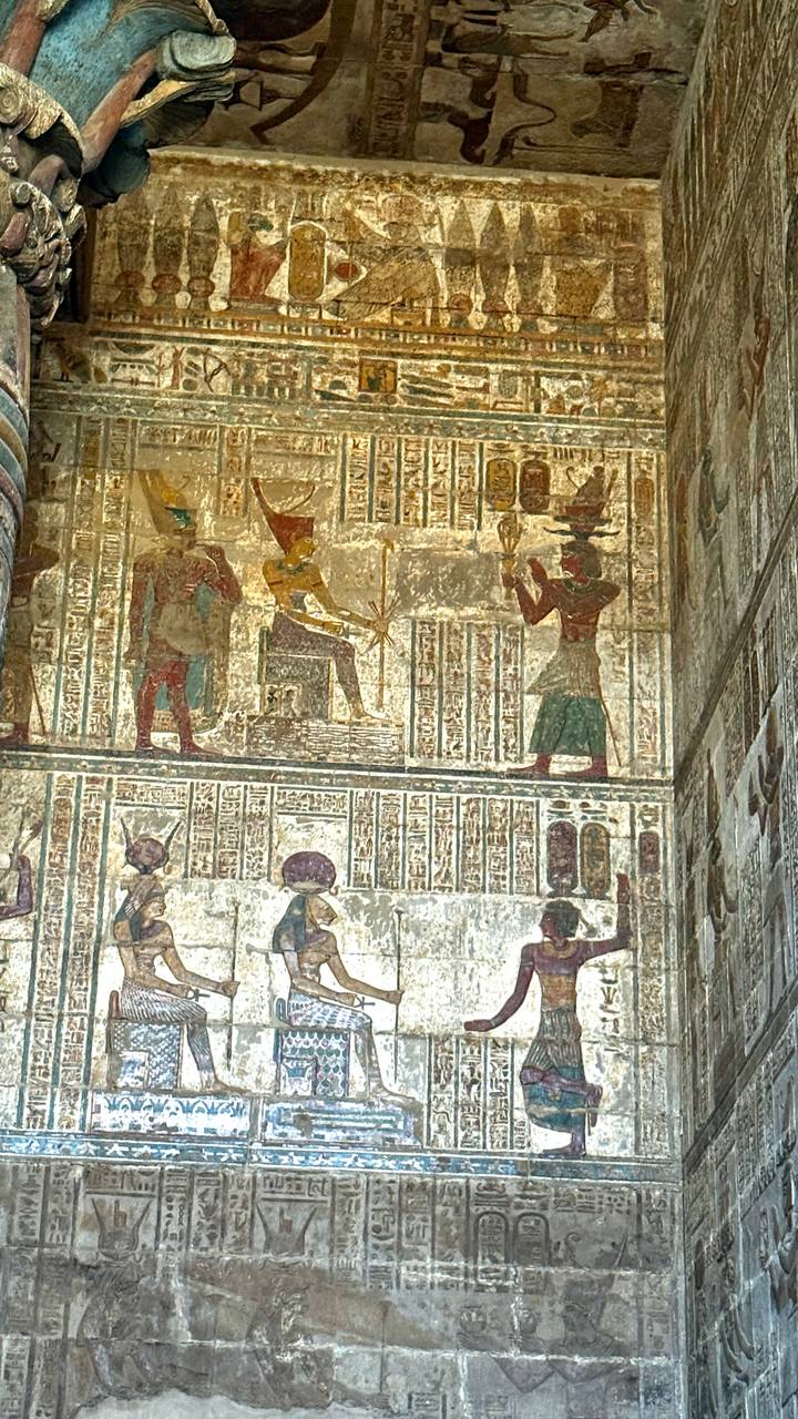 Vibrant wall panel with seated deity and hieroglyphic registers inside Egyptian temple.