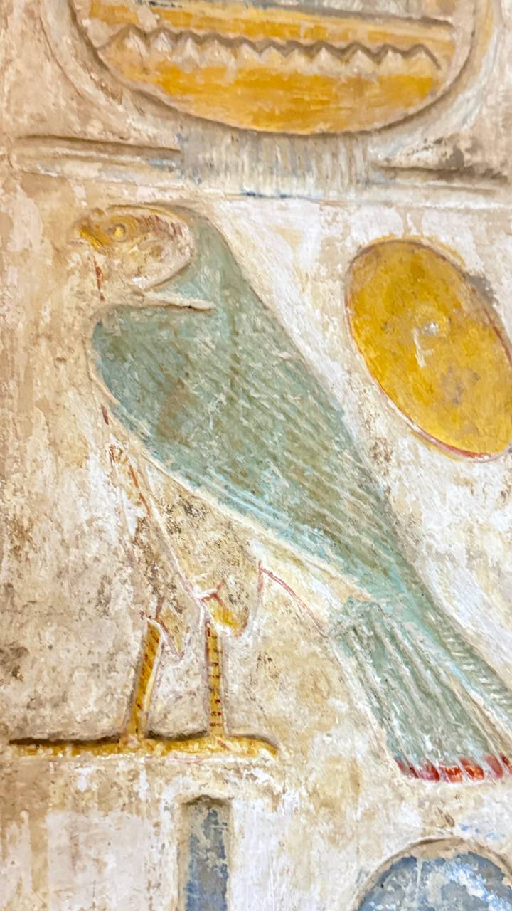 Blurry close-up of painted feather and yellow disk on ancient wall.
