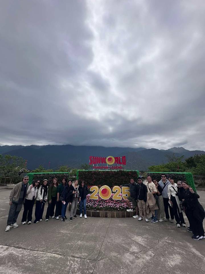 Group photo beneath a cloudy sky in front of the 'Sun World Fansipan Legend 2025' sign with mountains hidden in mist.