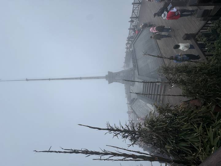 Visitors wander a mist-covered viewing deck and flagpole high in the mountains.