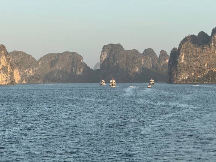 Tour boats cruise between dramatic limestone islands rising from emerald waters in Halong Bay.