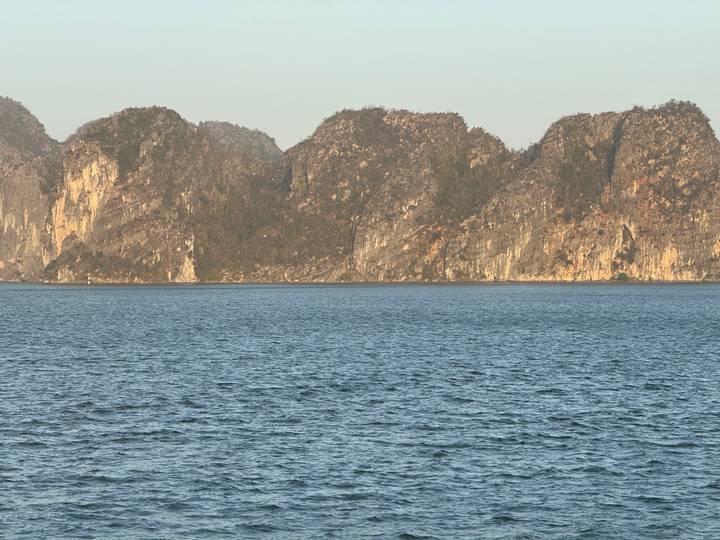 Sheer limestone cliffs rise from calm blue waters in late afternoon light.