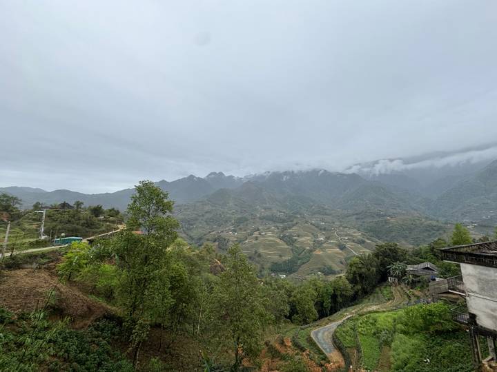 Overcast panorama of misty mountains and patchwork valleys dotted with small farms.