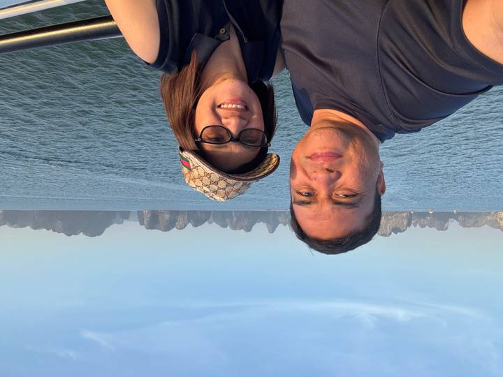 Smiling couple take a selfie on a boat with Halong Bay's karst peaks behind them.