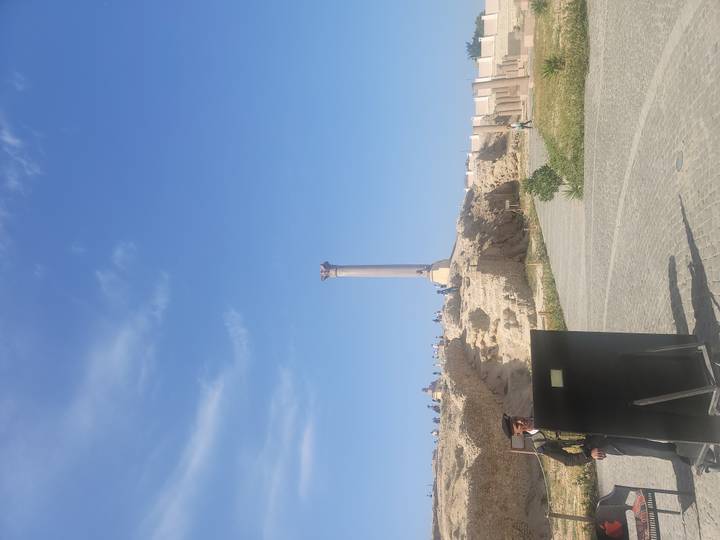 View of Pompey’s Pillar rising above ancient ruins under clear blue sky.