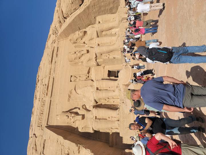 Tourists gathered before the colossal statues of Abu Simbel Temple carved into sandstone cliff.