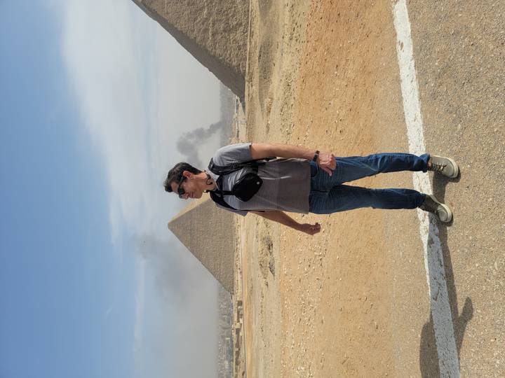 Man standing in front of the Great Pyramid with plumes of smoke in distant sky.