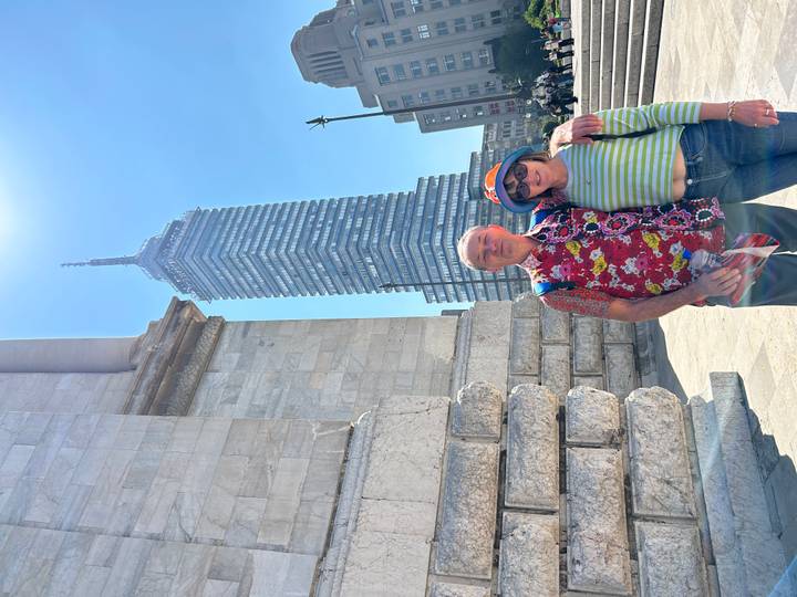 Couple stands beside a historic stone building with the Torre Latinoamericana skyscraper rising in the background.