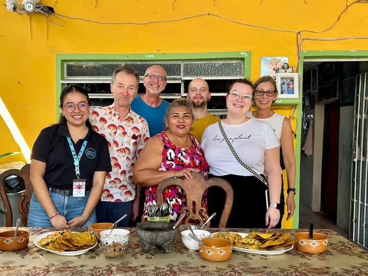 Group of travelers and locals smiling around a table after sharing a home-cooked meal in a brightly painted room.