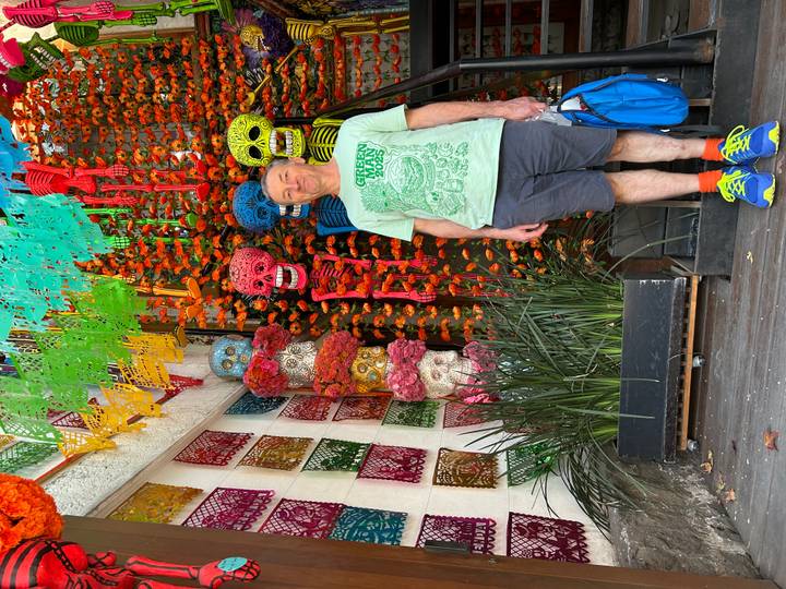 Man stands among colorful paper skull decorations and marigolds celebrating Day of the Dead.