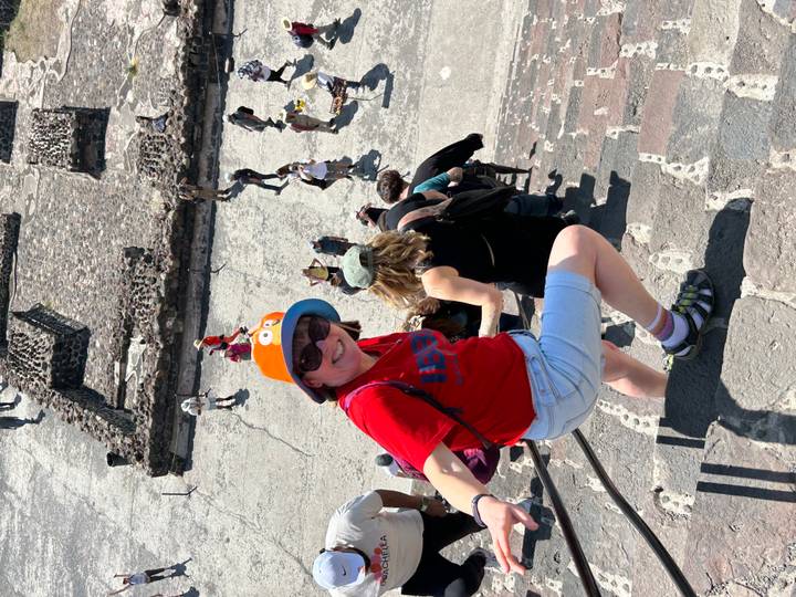 Woman climbing steep stone steps of an ancient pyramid with aerial view of the archaeological site below.