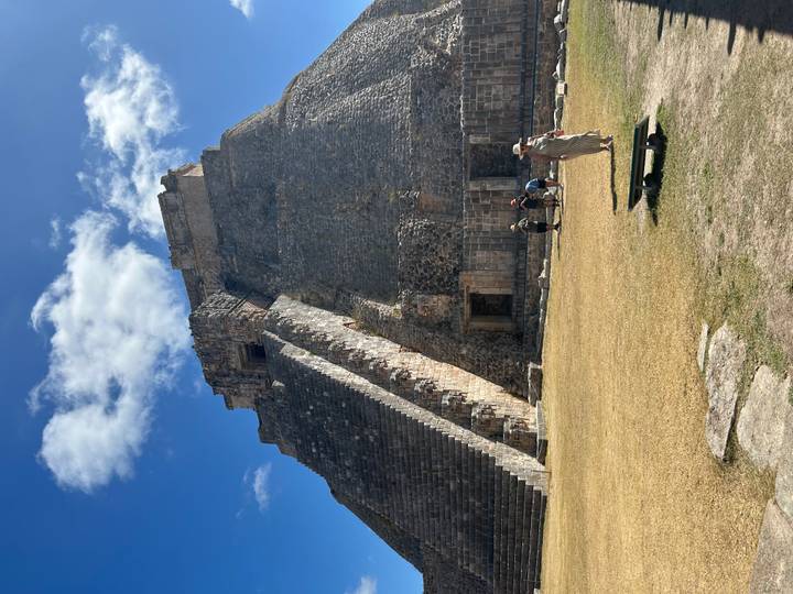Majestic Pyramid of the Magician at Uxmal rises under a bright blue sky with visitors at its base.