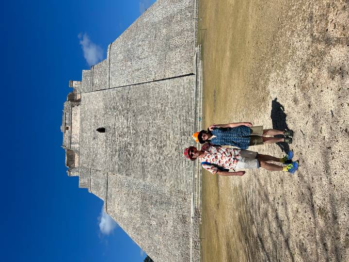 Couple stands in front of the massive stone pyramid at Uxmal under a deep blue sky.