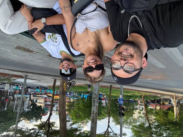 Three friends enjoy an open-air ride through Hanoi, smiling with city life in the background.