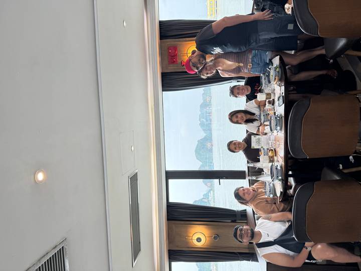 Friends share a meal at a window-side table on a Halong Bay cruise ship with karst views.