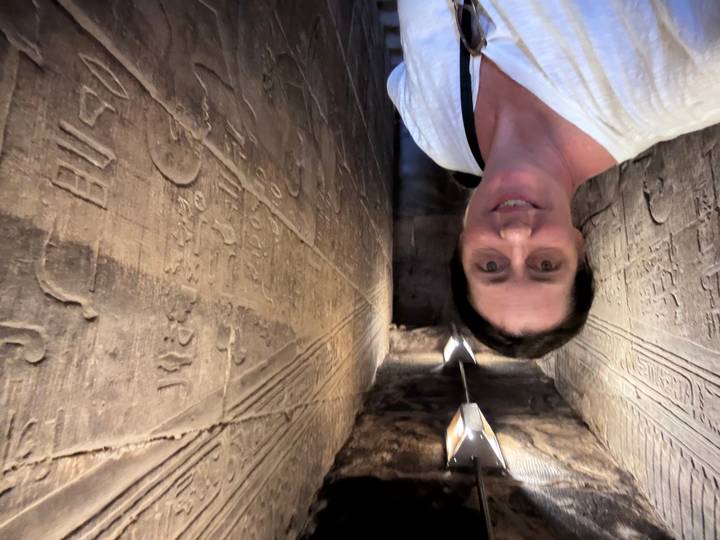 Visitor inside a narrow hieroglyph-covered corridor within an ancient Egyptian temple.