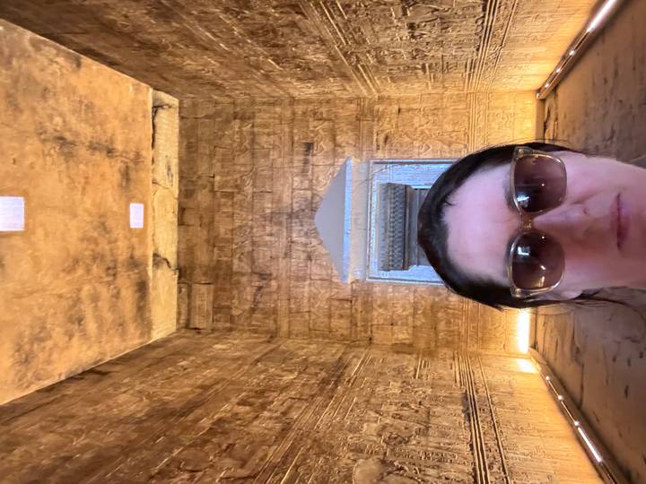 Close-up selfie in a dimly lit temple chamber adorned with golden hieroglyphs.