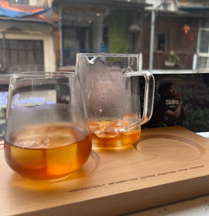 Close-up of chilled amber coffee drinks in glassware on a wooden tray at a Hanoi café window.