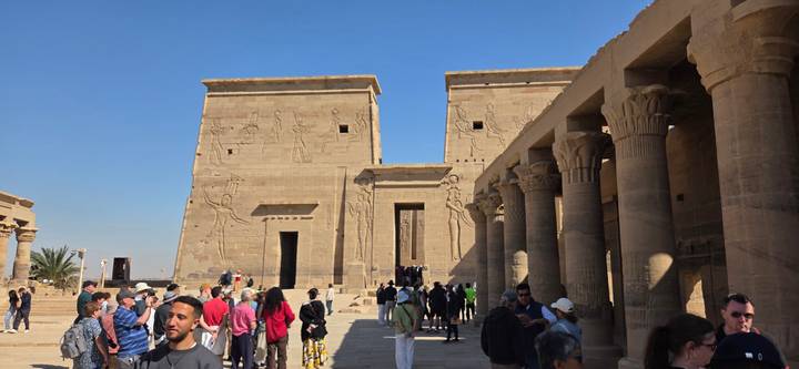 Tourists exploring the columned courtyard of Philae Temple with carved reliefs