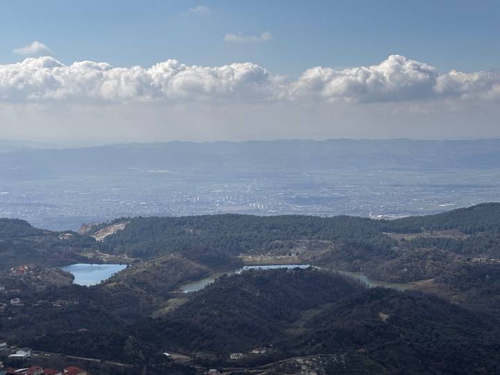 Wide vista of Tirana valley with lakes and cityscape beneath rolling mountain ranges and cloud banks.