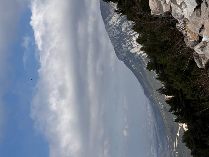 Mountain slope covered in evergreen forest beneath dramatic clouds with a glimpse of the plain below.