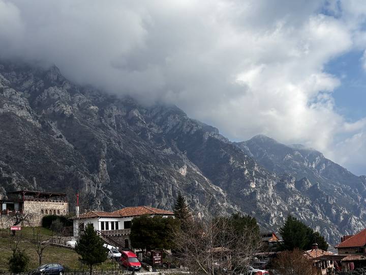 Dramatic rocky mountain range partially shrouded in low clouds with traditional stone houses at its base.