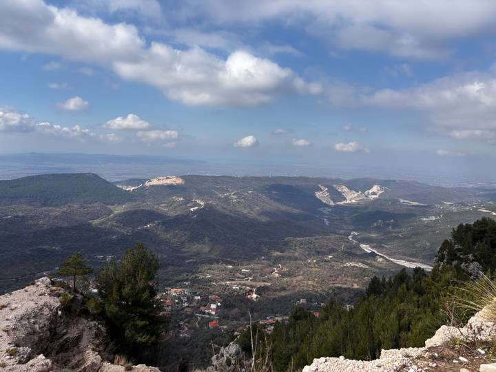 Wide panoramic view of a green valley and distant plains seen from a high mountain ridge on a bright day.