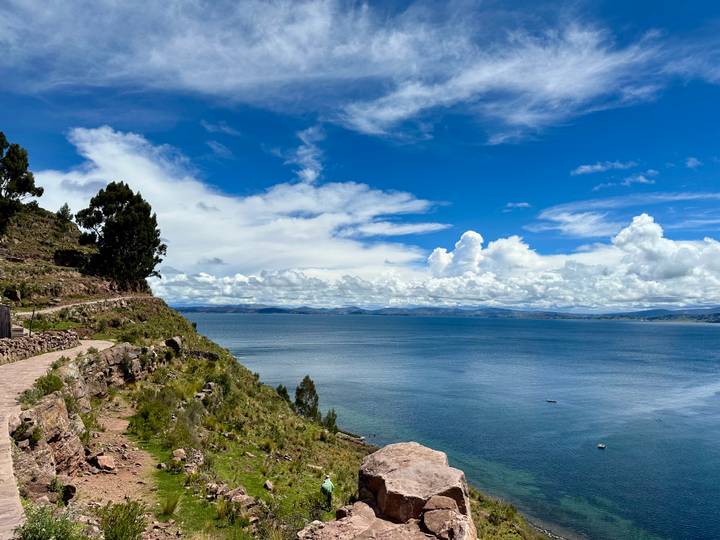 A coastal trail skirts the deep blue waters of Lake Titicaca beneath a sky of dramatic clouds.