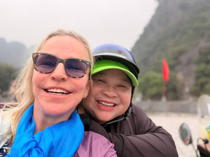 Close-up selfie of two smiling women with misty limestone hills in the background.