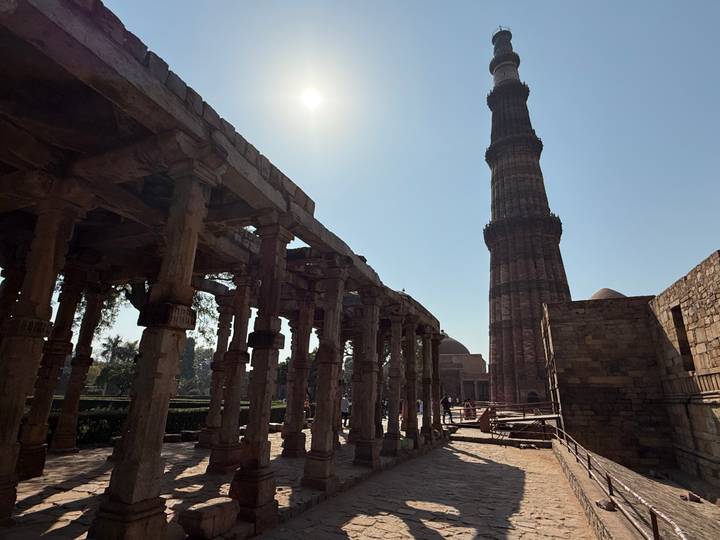 Silhouetted Qutub Minar and ancient columns under bright sun