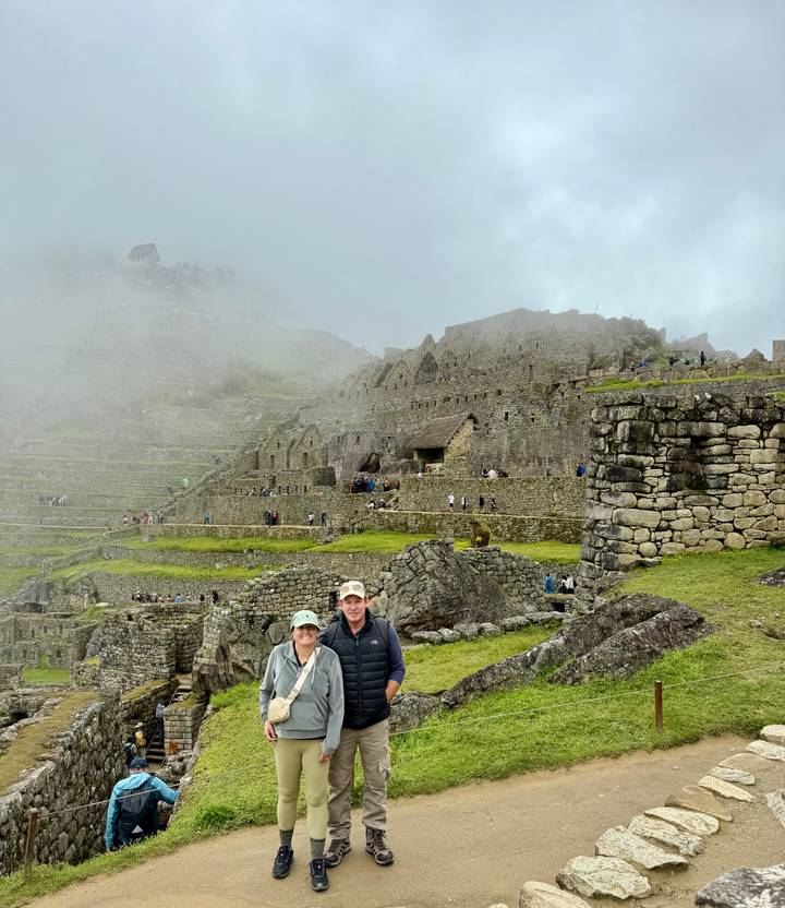 Smiling couple posing amid the misty stone terraces of Machu Picchu.