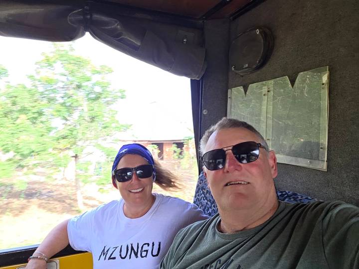 Selfie of two travelers wearing sunglasses inside a moving safari truck.