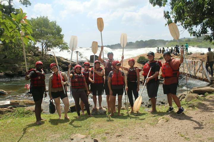 White-water rafting team posing with paddles beside powerful rapids.