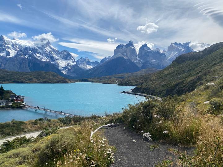 Turquoise lake framed by dramatic snow-capped peaks and a small lodge in Torres del Paine.